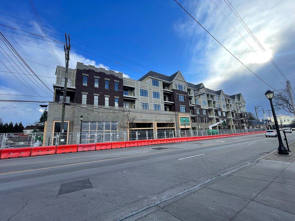 Four-story mixed-use commercial building under construction, with brick, stone and siding exterior, storefront openings and new windows, seen from across the street